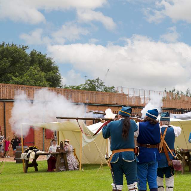 Historical reenactors firing muskets during Founder's Day at Colonial Fort Conde in Mobile, AL.