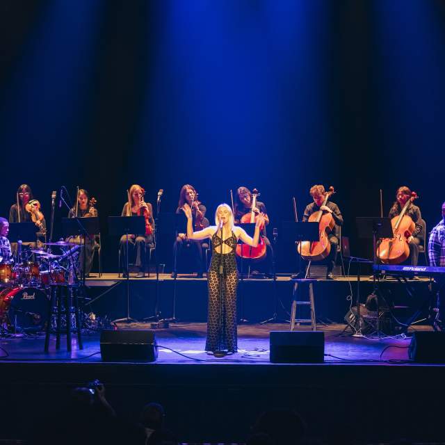 Grace Weber singing at a stand up mic with a string octet behind her