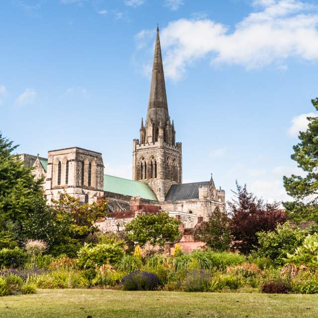 A view of Chichester Cathedral from the gardens with the spire reaching blue sky