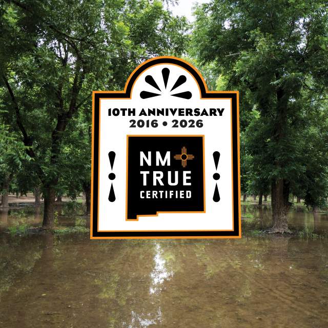 A forested area with partially submerged trees in floodwater is shown. There is a large logo displayed in the center, celebrating the 10th anniversary of "NM True Certified" from 2016 to 2026.