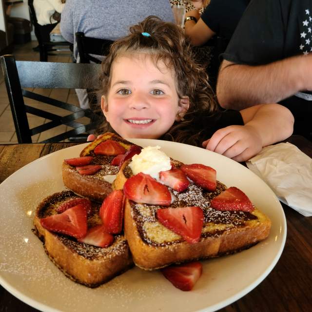 little girl with big plate of french toast covered in strawberries