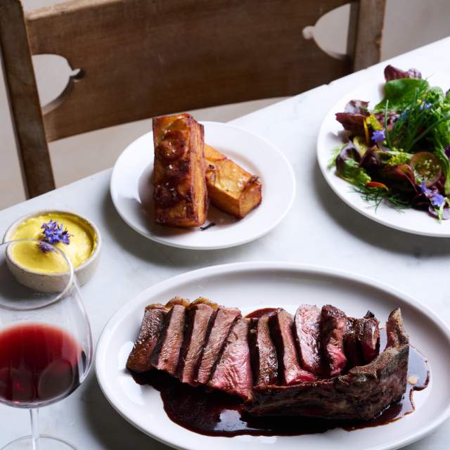 A table set up with plates of roasted meat, sides and a glass of red wine at Knepp Wilding Kitchen