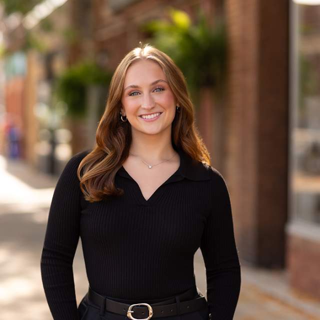 A white woman wearing all black, smiling and standing with her hands in her pocket.