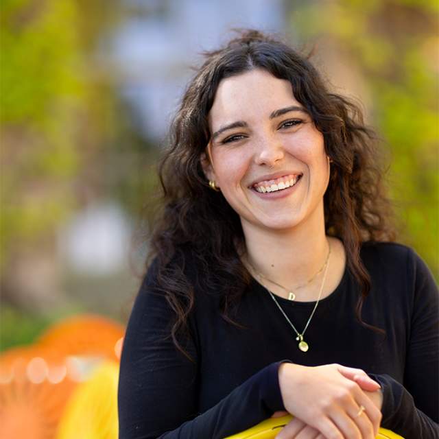 A white woman with dark curly hair smiling and sitting on a yellow terrace chair.