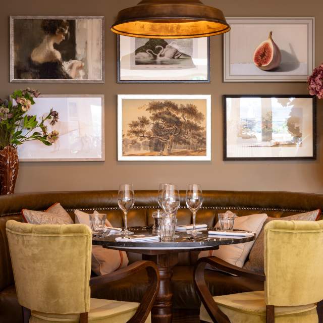 A dining table with banquette seats surrounded by artwork and flowers, at the White Hart in Lewes