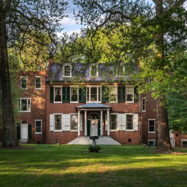 Exterior of a brick mansion with green trees framing the front entrance.