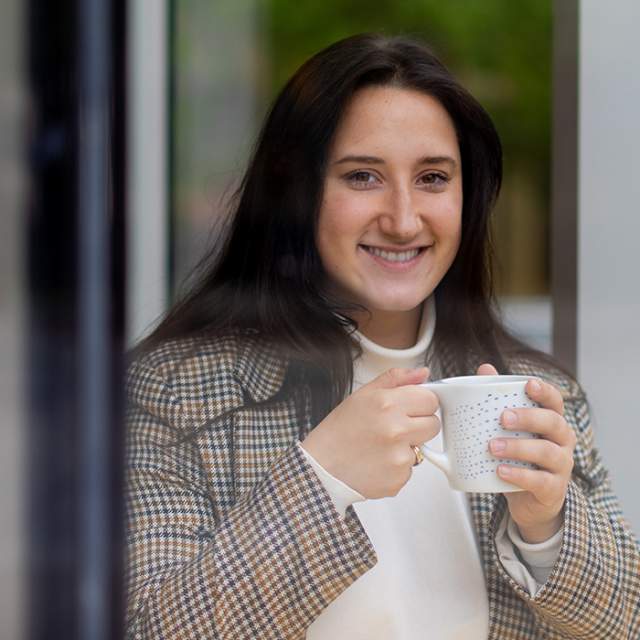 A woman sits in a window drinking coffee