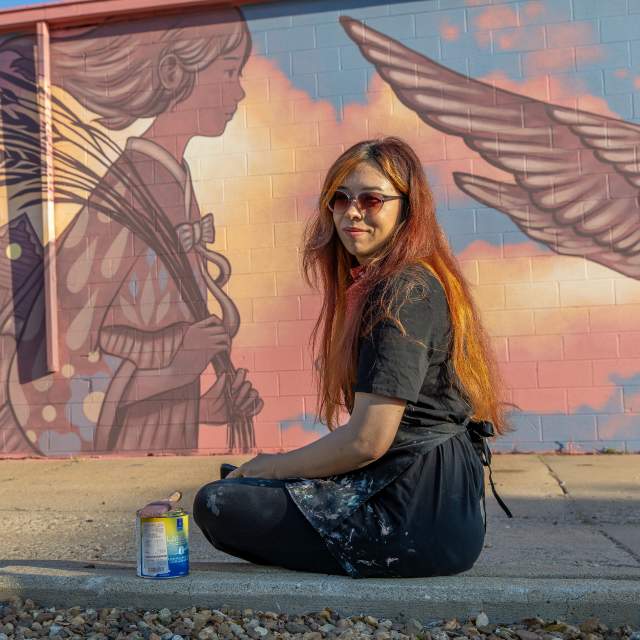 Amy Sol sits in front of her mural