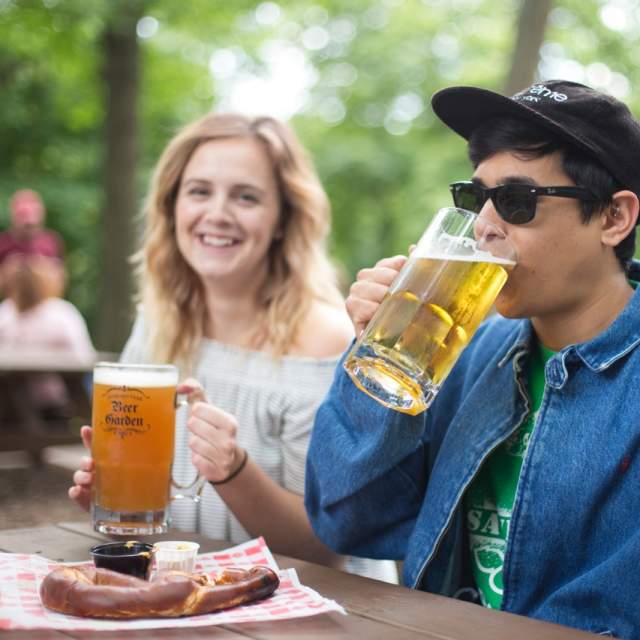 Two people at Hubbard Park Beer Garden, drinking beer over a large hot pretzel.