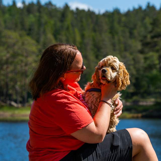 Dame som sitter med hunden på fanget ved ett tjern