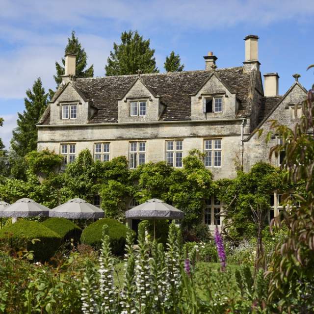 The stunning garden of The PIG - in the Cotswolds with umbrella shaded seating in front of the wisteria clad hotel
