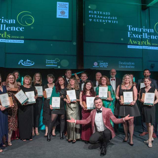 A group of people in fine dress holding their certificates and trophies in fromt of two large projector screens on a stage.