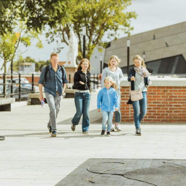 Family walking along Hull’s waterfront near The Deep, passing a large stingray sculpture embedded in the pavement on the Hull Fish Trail, with modern architecture and open public space creating a lively sightseeing atmosphere