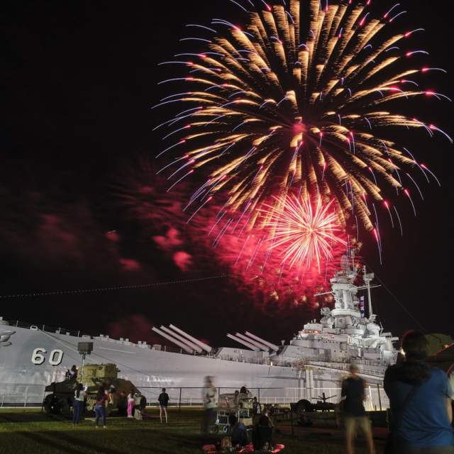 Red fireworks explode at night above the USS ALABAMA battleship