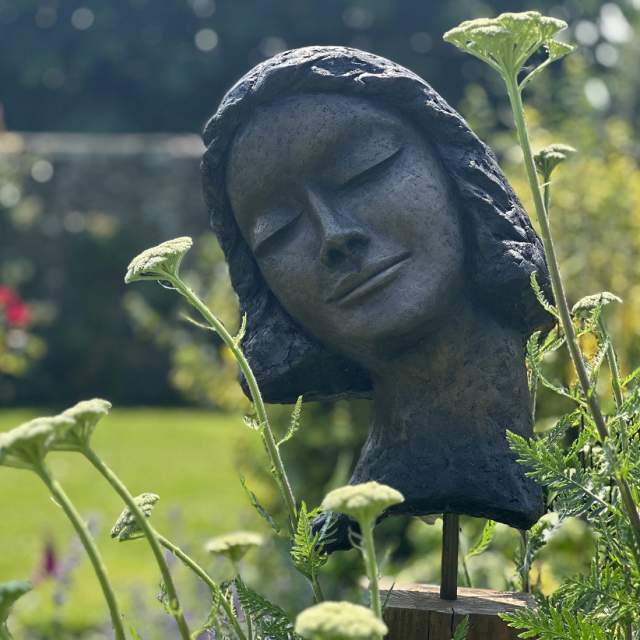 Sculpture of a head set amongst flowers and garden background