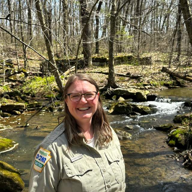 A woman posing for a photo in front of a stream in the woods