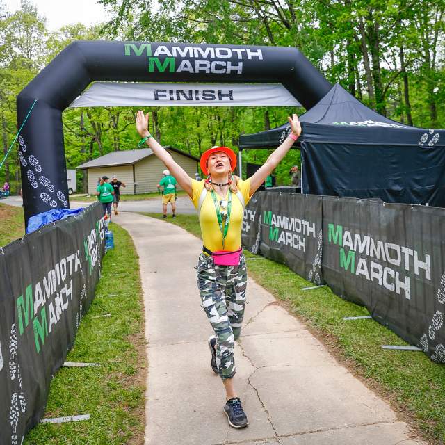 A woman celebrates with her hands in the air at the finish line of MammothMarch at Oak Mountain State Park.