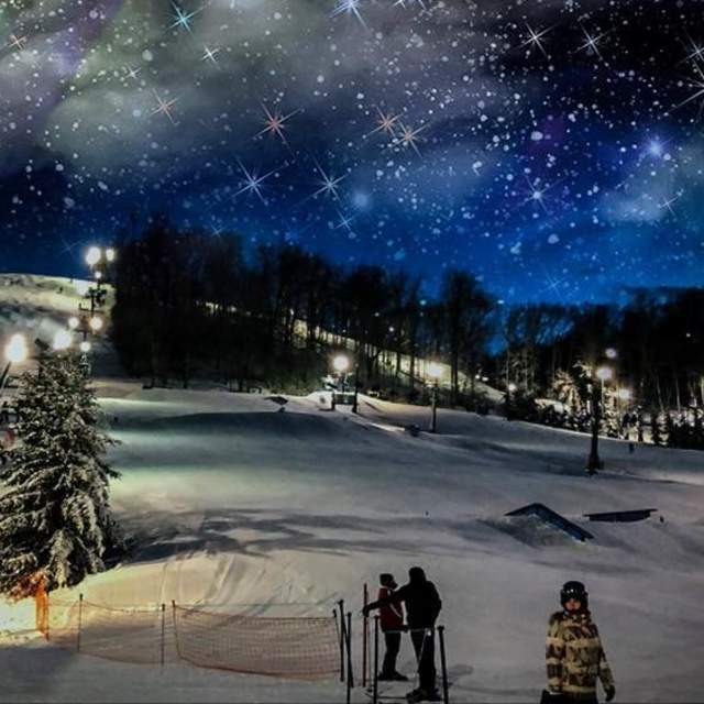 A snow covered slope under a starry sky with skiiers in the foreground and a ski lift at Perfect North in Indiana
