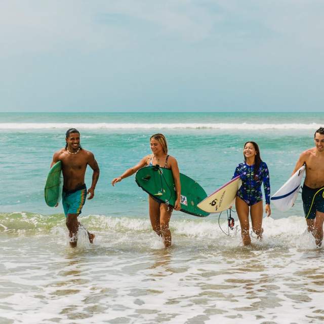 Cuatro surfistas divirtiéndose en las olas de Playa El Palmar, Riviera Pacífica, Panamá