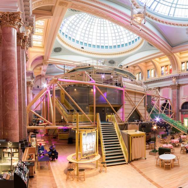 Inside the Royal Exchange Theatre with theatre space in the centre of the room and chairs and tavles set up outside