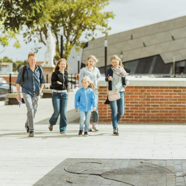 Family walking along Hull’s waterfront near The Deep, passing a large stingray sculpture embedded in the pavement on the Hull Fish Trail, with modern architecture and open public space creating a lively sightseeing atmosphere