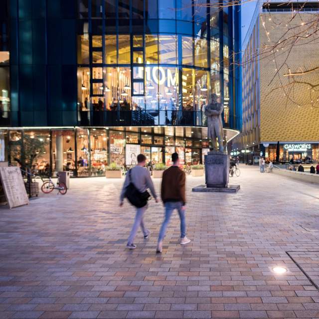 2 people walking in a square in front of HOME venue.
