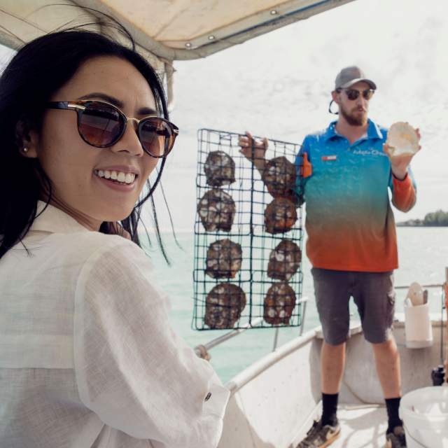 A Willie Creek Pearl Farm tour guide holds up a panel full of pearl shell, while tour guests look on