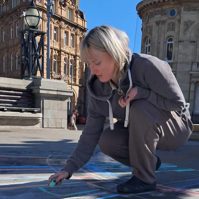 Ellie Seal dressed in a grey jumpsuit draws with chalk on the pavement