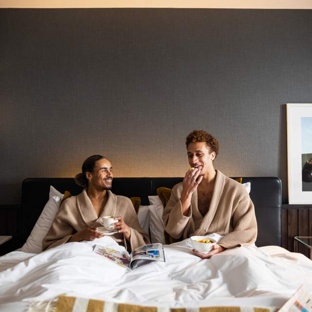 Couple in hotel bed in dressing gowns eating breakfast and drinking coffee