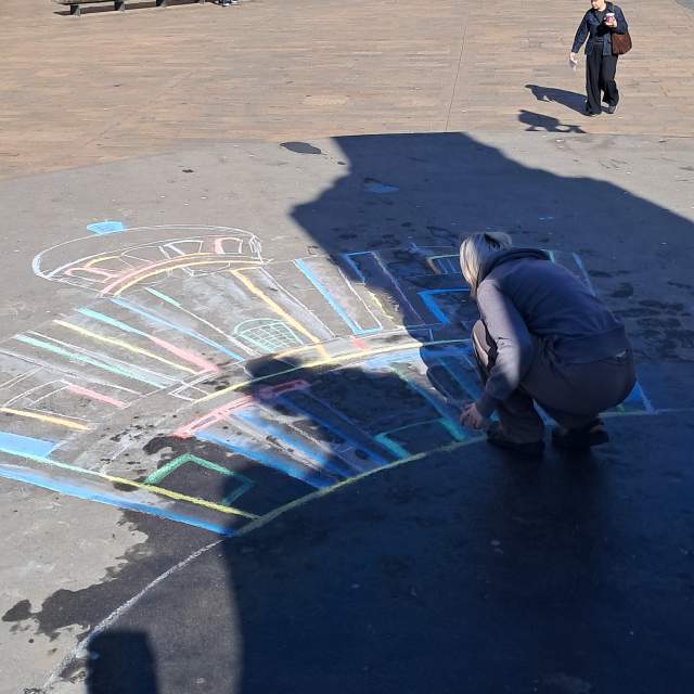 A young female draws Hull City Hall in chalk on the pavement in Queen Victoria Square