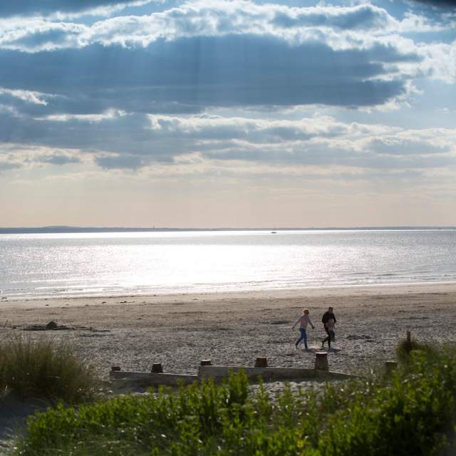 Sunny day at West Wittering beach looking out to sea, with a couple walking in the sandy dunes