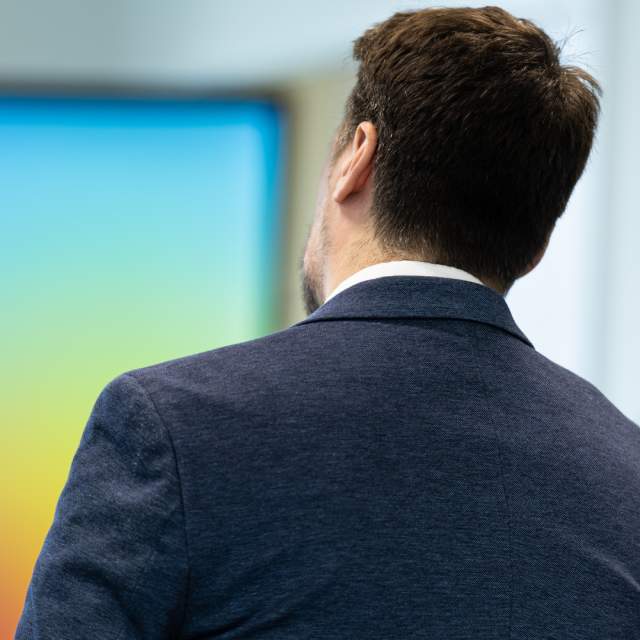 The back of a suited person looking towards a digital screen.