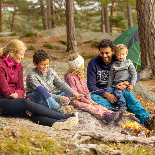 Familie på tur i skogen hvor de griller pølser.