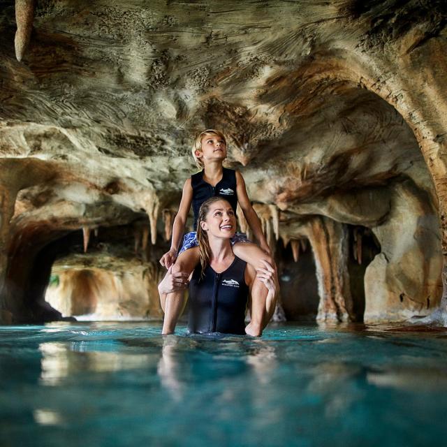 A mother with her son on her shoulders in a cave at Discovery Cove