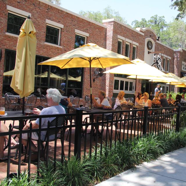 People sitting and drinking under umbrellas in outdoor dining area of Crooked Can Brewing Company at Plant Street Market in Winter Garden.