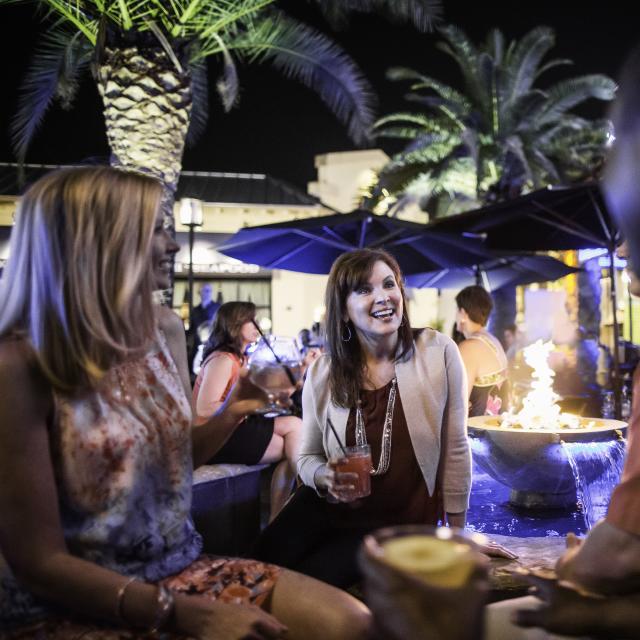 A group of four people having drinks outside of Blue Martini at night with a fire pit in the background