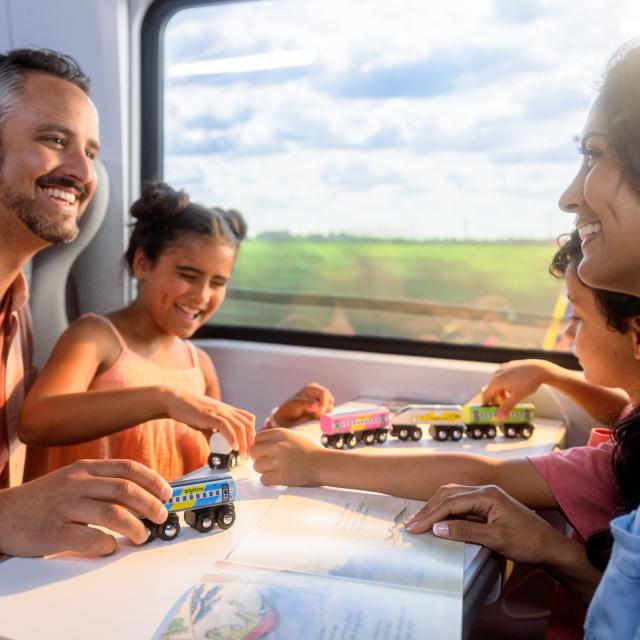 Family riding on Brightline train while kids play with toy train