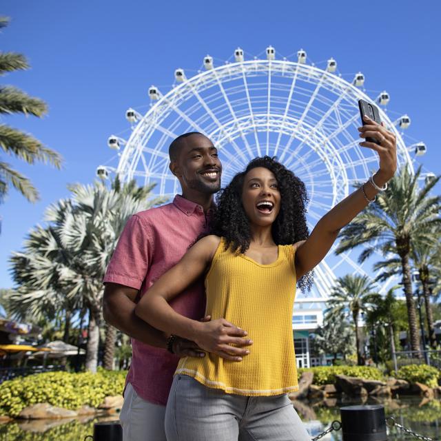 A couple posing for a selfie in front of The Wheel at ICON Park