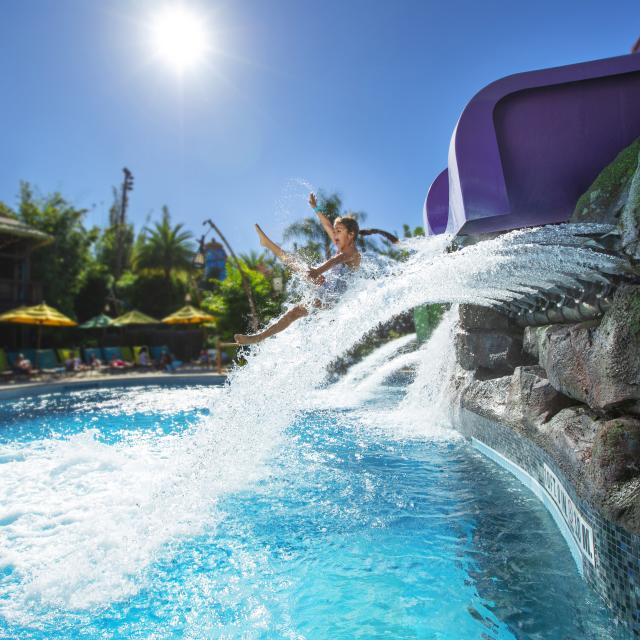 A little girl coming out of a water slide and dropping down into a pool at Universal's Volcano Bay.