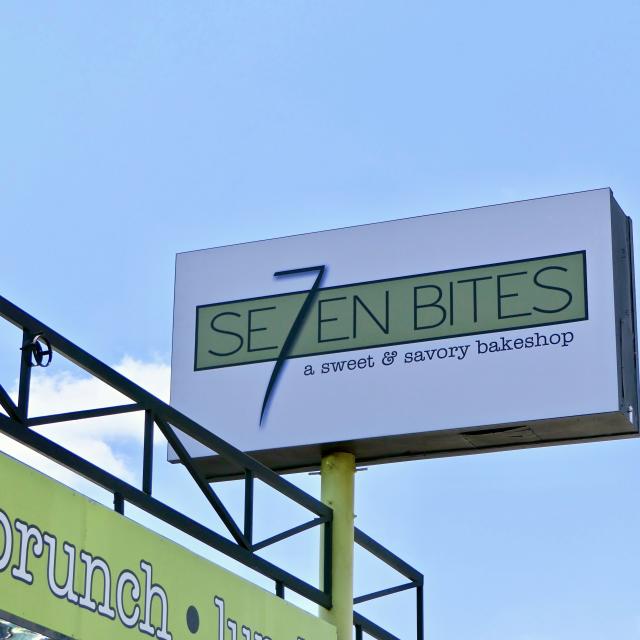 A large white and green sign with the Se7en Bites logo stands above a lime green arch, with blue skies behind it, in Orlando, Florida.