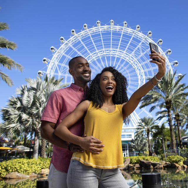 A couple posing for a selfie in front of The Wheel at ICON Park