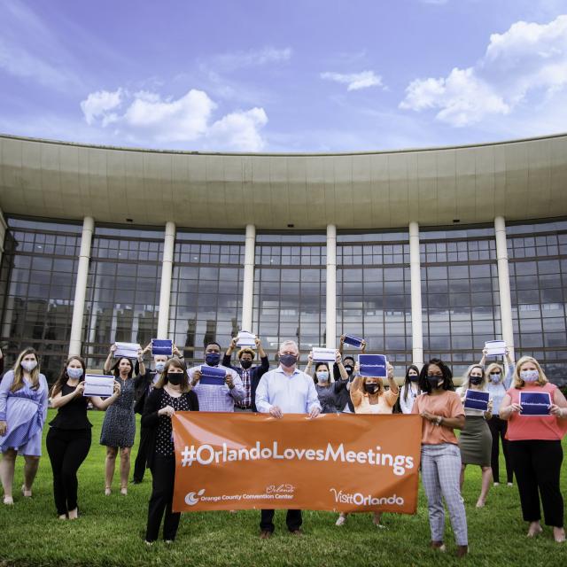 The Visit Orlando team holding a #OrlandoLovesMeetings banner in front of the Orange County Convention Center for Global Meetings Industry Day