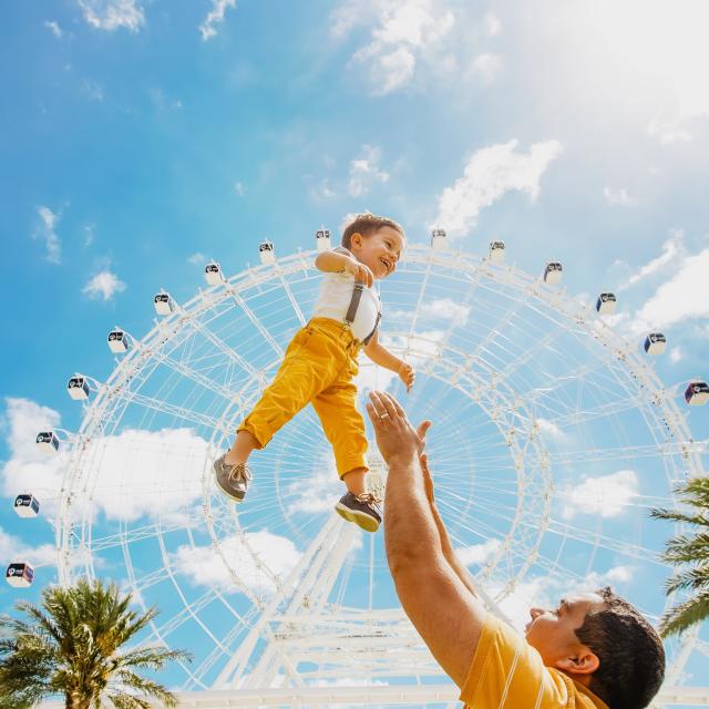 father throwing son up in air in front of The Wheel at ICON Park