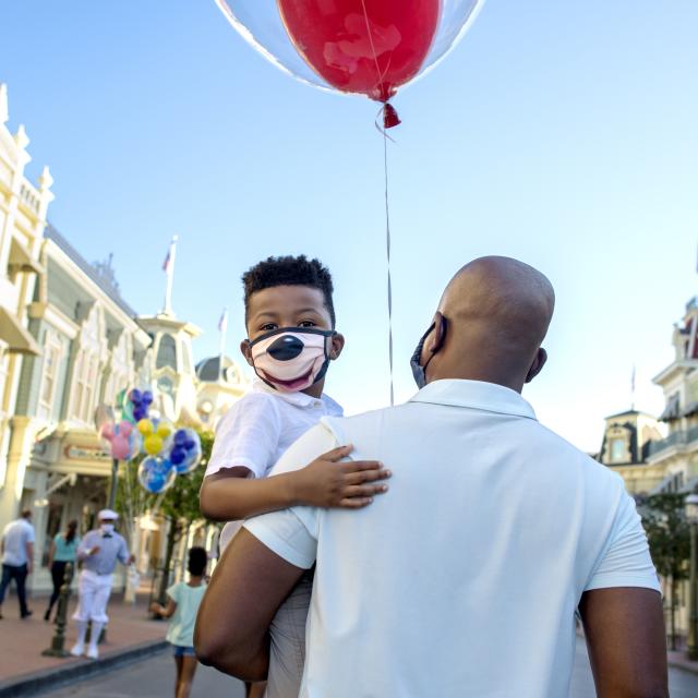 A father holding his son while walking down Main Street in the Magic Kingdom.