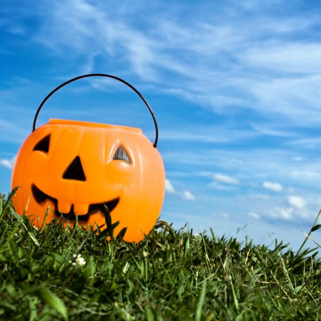Plastic pumpkin candy holder sitting in the grass under blue skies.
