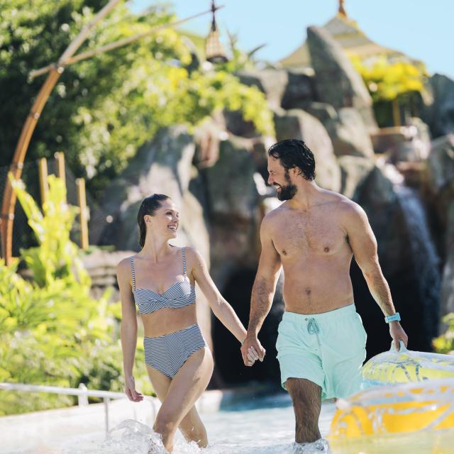 A couple holding hands as they are walking out of the lazy river in Universal's Volcano Bay