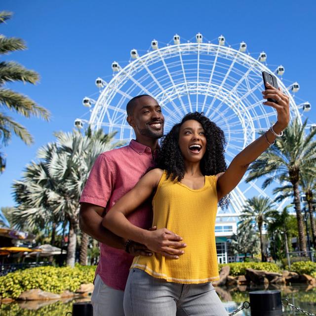 A couple posing for a selfie in front of The Wheel at ICON Park