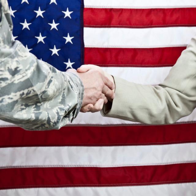 A handshake between a member of the military and a female civilian with an American flag background