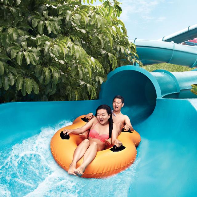 A young couple exit the barrel of a slide while riding on a double ring float