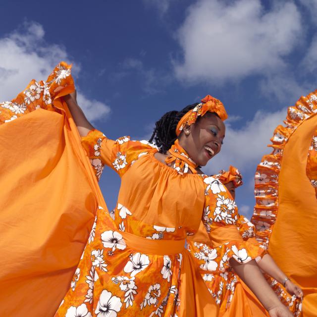 Caribbean dancing troupe wearing bright orange costumes perform on a beach.
